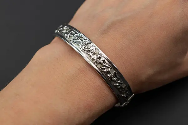 Silver bracelet on a female hand on a black background close-up