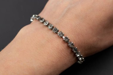 Siyah arka planda bir kadının elinde elmas bilezik.