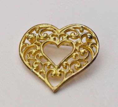 Beyaz arkaplanda altın kalp şeklinde broş, yakın plan.
