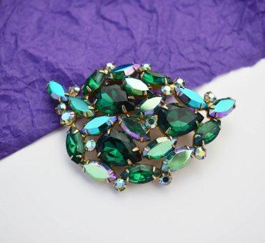 Beyaz arka planda zümrütleri olan mücevher broşu.