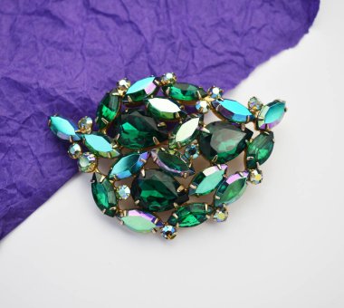 Beyaz arka planda zümrütleri olan mücevher broşu.