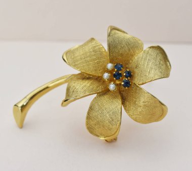 Beyaz arka planda mavi değerli taşlı altın çiçekli broş.