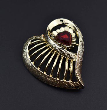 Siyah arka planda kırmızı kalpli altın broş. Mücevherler.