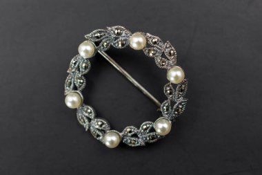 Siyah arka planda incili gümüş broş, yakın plan.