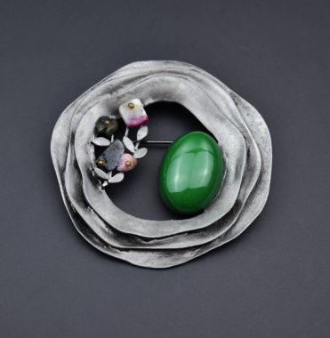 Yakından bir broş ve yeşil bir değerli taş.