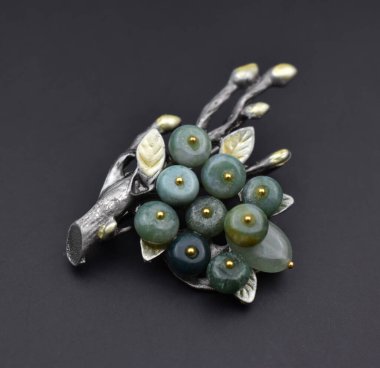 Siyah zemin üzerinde yeşil ve mavi değerli taşlar olan mücevher broşu.