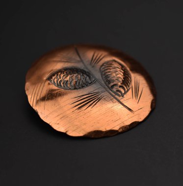 Siyah bir zemin üzerinde bulanık arkaplanı olan bakır bir broşun yakın plan çekimi.