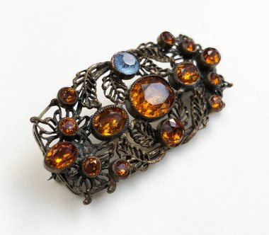 Beyaz arkaplanda siyah ve turuncu taşlardan yapılmış bir broş.