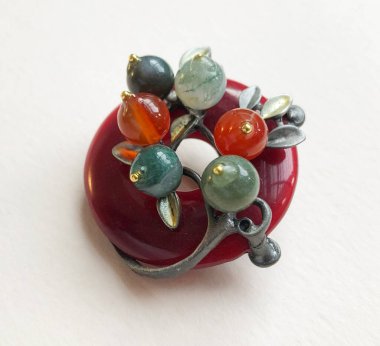 Beyaz arka planda kırmızı ve yeşil boncuklardan yapılmış mücevher broşu.