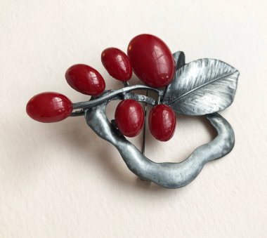 Beyaz arka planda metal bir broşun içindeki kızılcıklar.