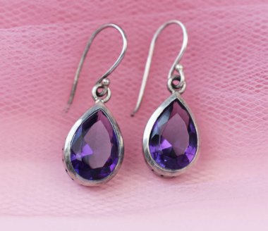 Pembe arka planda mor ametist kristalleri olan gümüş küpeler..