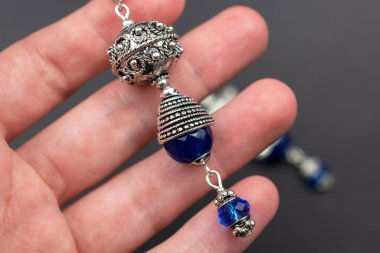 Siyah arka planda gümüş ve mavi bir küpe tutuyor..