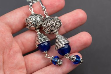 Siyah arka planda mavi ve gümüş taşlı el ele tutuşan küpeler.