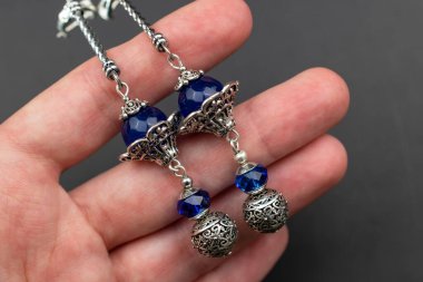 Elinde bir çift mavi ve gümüş küpe, yakın çekim.