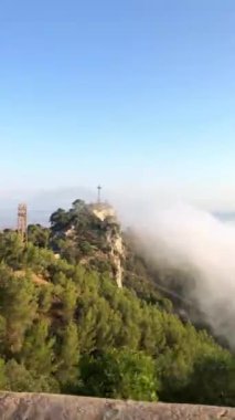 Bir dağın tepesinden bulutların altındaki bir vadiye doğru dikey bir tarama yapan bir video..