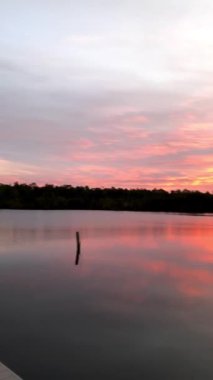 Gün batımı ışığı, nehir ve ormanla çevrili sakin bir göle yansıyor..