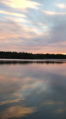 Sakin göl, orman ve nehir tarafından çerçevelenmiş canlı günbatımı gökyüzünü yansıtır..