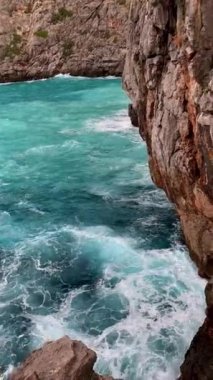 Büyük dalgalar sessiz bir plajda kayalara çarpıyor, büyüleyici doğal manzara.