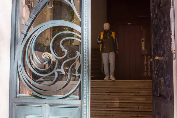 Bir yemek teslimatçısı ahşap bir kapının önünde duruyor ve ona bakıyor..