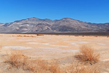Açık mavi gökyüzünün altında dağları olan çöl manzarası..