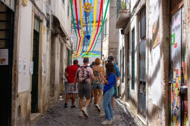 Portekiz, Lizbon 'da dar bir sokakta renkli kurdeleler altında yürüyen insanlar..