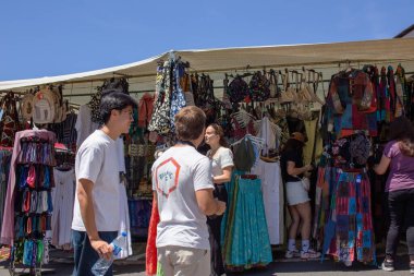 İnsanlar güneşli bir günde canlı bir açık hava pazarında kıyafetlerini karıştırıyorlar.