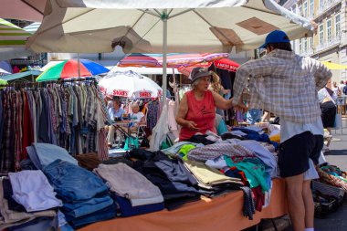 Satıcıların ve müşterilerin kıyafetleri karıştırdığı canlı bir sokak piyasa sahnesi.