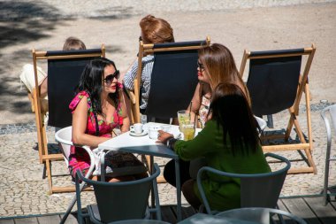 Bir grup arkadaş güneşli bir yaz gününde bir kafede yemek yiyorlar.