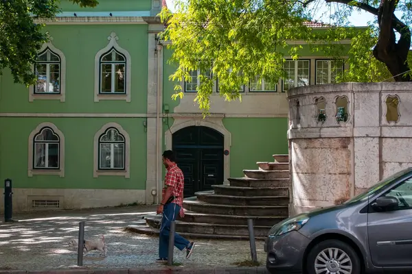 Yeşil bir binanın önünde merdivenleri olan bir köpekle yürüyen adam.