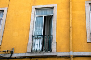 Canlı sarı bir binanın ön cephesinde balkonlu bir pencere.