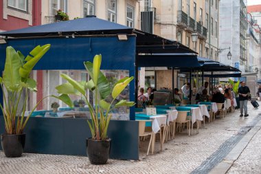 Mavi tenteli ve saksı bitkilerli açık hava restoranı.