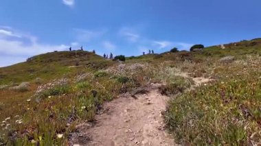 Atlantik dalgaları ve açık gökyüzü ile Portekiz 'in kayalık yamaçlarından yürüyüşçüyü izle