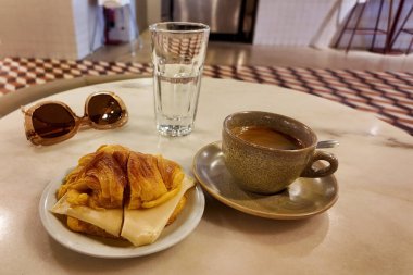 Kahve, kruvasan ve mermer bir masada güneş gözlüğü.
