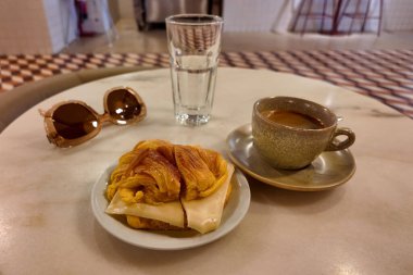 Kafe masasında kahve, kruvasan ve aksesuarlarla kahvaltı sahnesi..