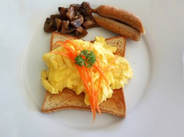 Kızarmış ekmeğin üstünde yumurta ve beyaz tabakta sosis.