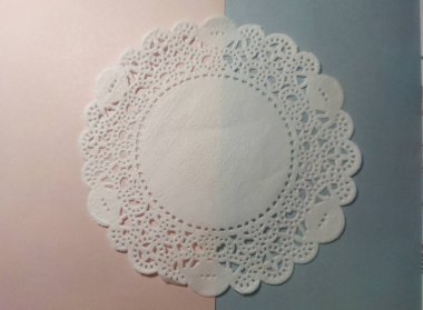 White perforated and textured of doily or dolly paper on pink and blue background clipart