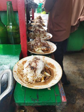 Plates of ketoprak dish being prepared by seller, Ketoprak dish consists of tofu, vegetables and rice cake, rice vermicelli served in peanut sauce clipart