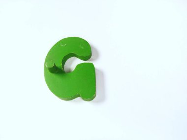 Yakın çekim, beyaz üzerinde izole edilmiş, G harfi şeklinde saf, parlak sarı tahta bir nesne içerir.