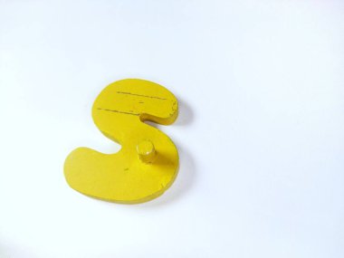 Yakın plan çekimde, beyaz üzerine izole edilmiş S harfi şeklinde saf, parlak sarı tahta bir nesne bulunur.