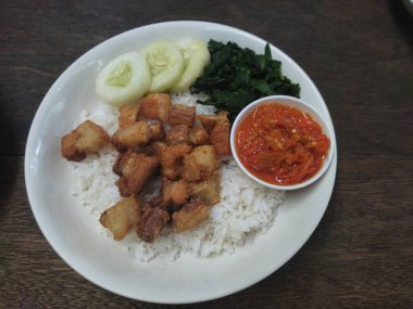 Beyaz pirinçli, kızarmış domuz göbeği küplü, canlı kırmızı acı biberli, kavrulmuş kaju yaprağı ve taze salatalık dilimleriyle servis edilen Endonezya yemeği.