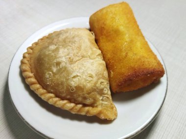 Yakın plan çekimlerde beyaz bir tabakta iki altın sarısı kızarmış atıştırmalık bulunur: köri veya pastel ve bir börek.