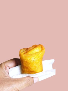 Bir el beyaz kağıt peçetede tek bir altın sarısı, kızarmış rissole tutar. Yakın çekim düz pembe arka plan ile dokuyu vurguluyor.