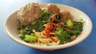 Köfteli şehriye çorbası erişte, bir büyük köfte, üç küçük köfte ve sebzeden oluşan beyaz bir kâseye yakın.