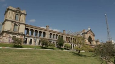 Alexandra Sarayı, güneşli bir günde Londra. Kamera ana cephede yankılanıyor. Kırmızı bir Londra otobüsü geçiyor. 16x9 manzara geniş açı.