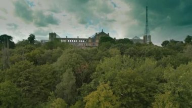 Bulutlu bir günde Alexandra Sarayı. Kamera, Londra 'daki Alexandra Sarayı' nın ana perdesini ortaya çıkarmak için ağaçların üzerinde ileri geri hareket ediyor. Kara kara düşünen bulutlar. 16x9 manzara geniş açı.