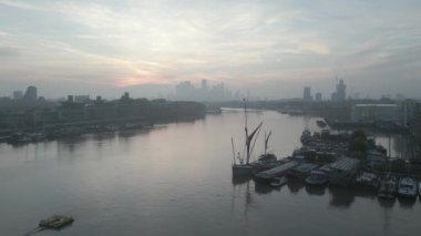 Londra 'da Thames Nehri' nde şafak vakti. Bir 19. yüzyıl yelkenli mavnası gökyüzüne karşı gölgelenmiştir. Yakınlarda Butlers Wharf, Concordia Wharf ve St Saviours Rıhtımı var. Uzakta Kanada Meydanı 'ndaki Docklands gökdelenlerinin sisli silueti var.