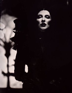 Glamorous female vampire stands in front of a spooky gothic window (1 of 4). Dark atmospheric lighting, the black and white photo taken with 19th century chemical process called wetplate collodion clipart