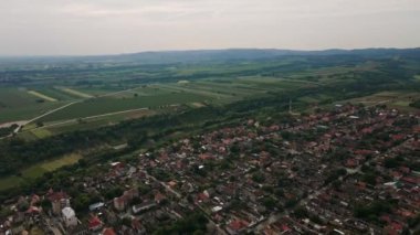 Bulutlu kış gününde tarımsal tarlaları olan bir köyün, arka planda duran tepelerin hava görüntüleri.