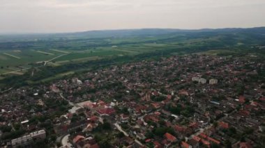 Bulutlu kış gününde tarımsal tarlaları olan bir köyün, arka planda duran tepelerin hava görüntüleri.