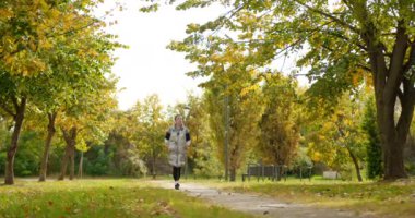 Güzel genç bir kadın güz gününde neşeyle parkta yürür.